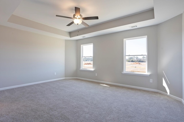 carpeted empty room with a tray ceiling, a ceiling fan, visible vents, and baseboards