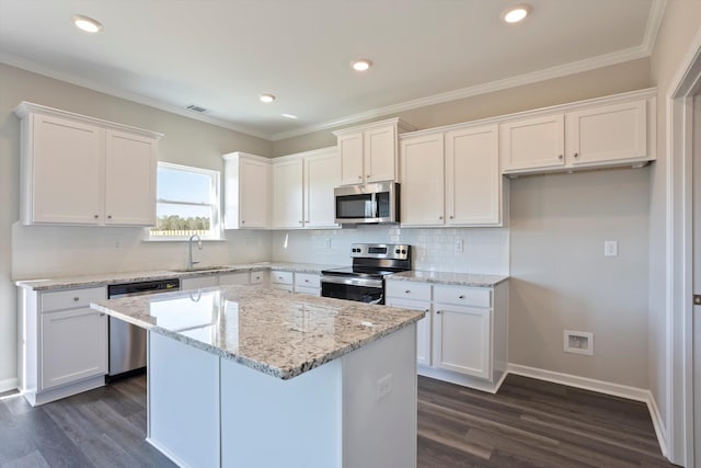 kitchen with a sink, white cabinetry, appliances with stainless steel finishes, a center island, and crown molding