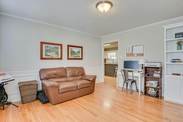 living area featuring crown molding, light wood-style flooring, wainscoting, and a textured ceiling