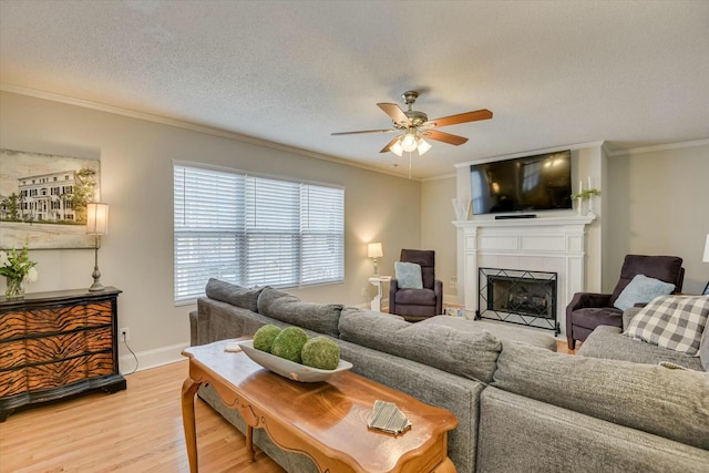 living area featuring a tiled fireplace, crown molding, light wood finished floors, and ceiling fan