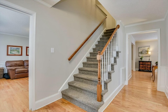 stairway with crown molding, wood finished floors, visible vents, and baseboards