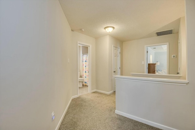 corridor with light carpet, visible vents, a textured ceiling, and baseboards