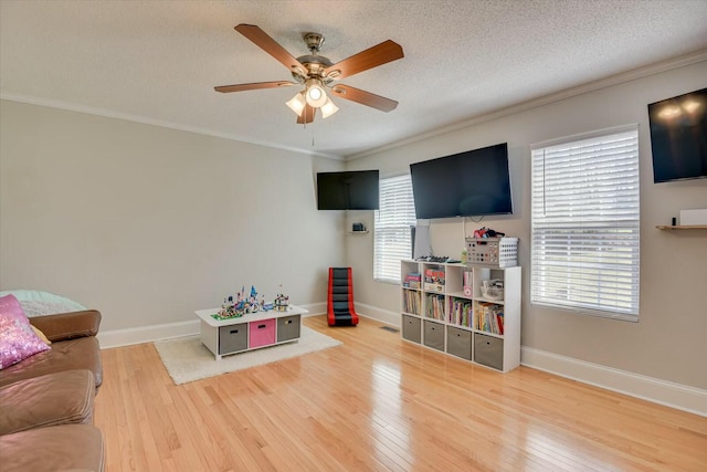 living area featuring hardwood / wood-style floors, a ceiling fan, baseboards, a textured ceiling, and crown molding