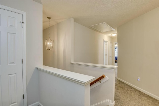 hall featuring baseboards, attic access, a textured ceiling, an upstairs landing, and light colored carpet