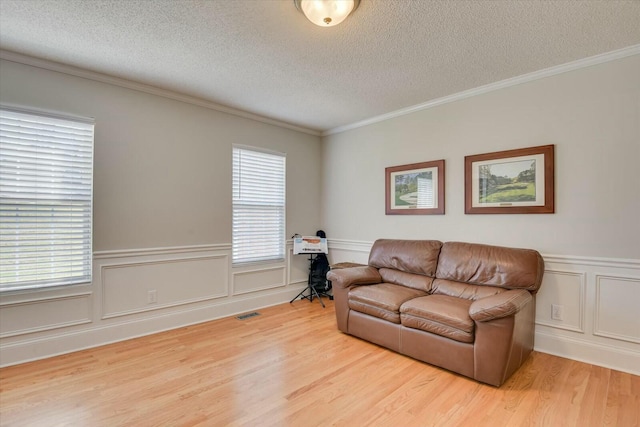 living room featuring a textured ceiling, light wood-style flooring, and crown molding