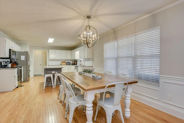 dining space with a notable chandelier, a textured ceiling, light wood-style floors, wainscoting, and crown molding