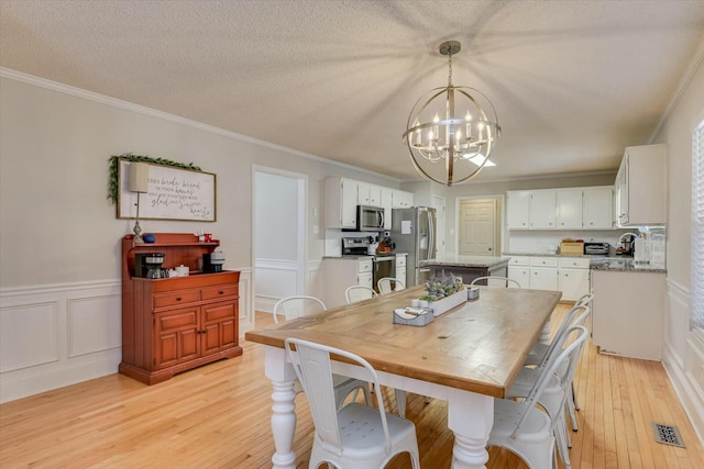 dining room featuring crown molding, a chandelier, a wainscoted wall, light wood-type flooring, and a textured ceiling