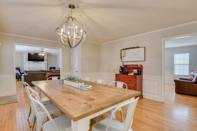 dining area featuring light wood-type flooring, a wainscoted wall, ornamental molding, a textured ceiling, and a fireplace