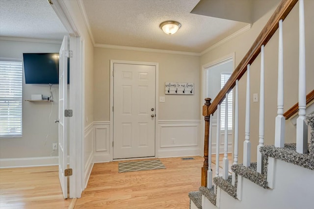 foyer entrance with light wood-type flooring, stairs, and ornamental molding