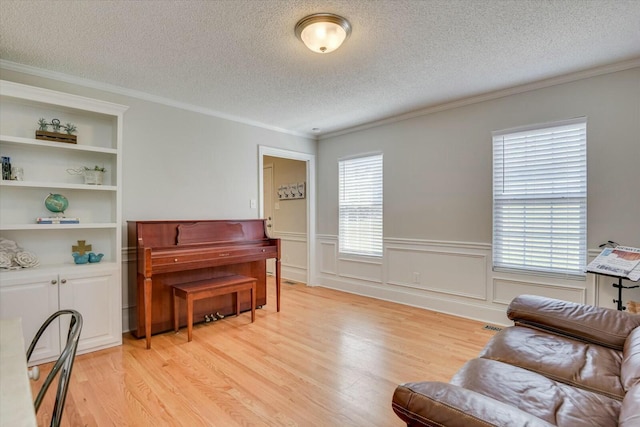 living area featuring a textured ceiling, wainscoting, light wood finished floors, and ornamental molding