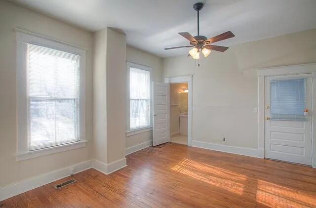 unfurnished bedroom featuring ensuite bath, ceiling fan, hardwood / wood-style floors, and multiple windows