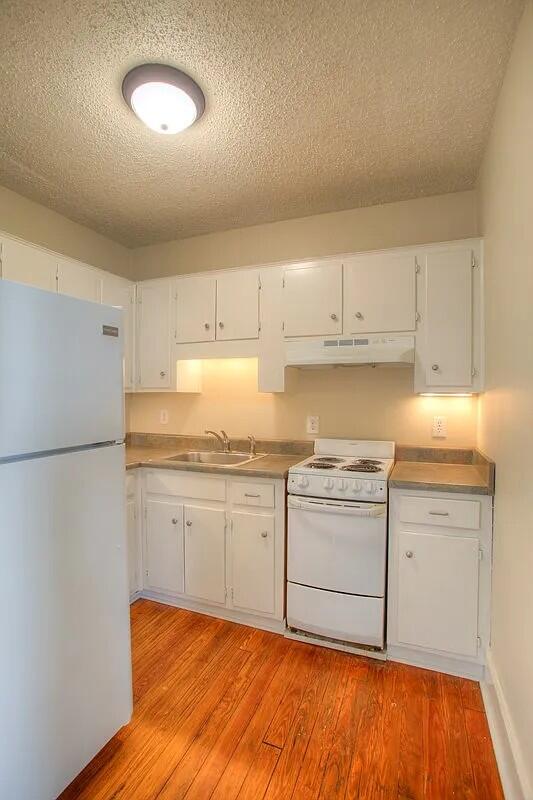 kitchen with light wood-type flooring, a textured ceiling, white appliances, sink, and white cabinets