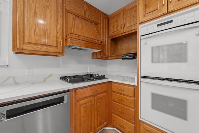 kitchen with light stone counters, stainless steel appliances, and custom range hood