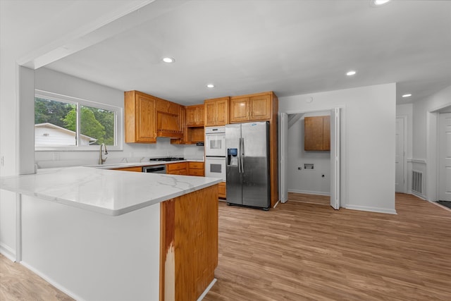 kitchen with sink, kitchen peninsula, light hardwood / wood-style flooring, double oven, and stainless steel fridge with ice dispenser