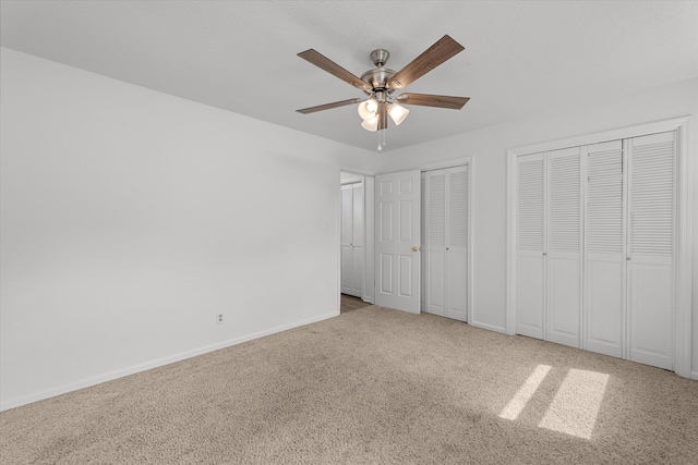 unfurnished bedroom with light carpet, two closets, and ceiling fan