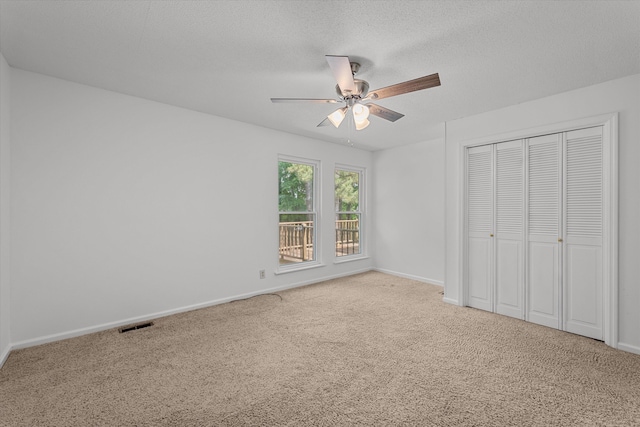 unfurnished bedroom featuring ceiling fan, a closet, light colored carpet, and a textured ceiling