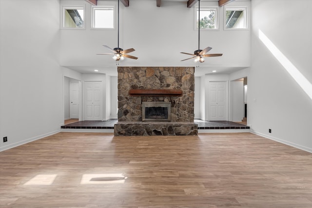 unfurnished living room featuring a fireplace, a high ceiling, light wood-type flooring, and ceiling fan