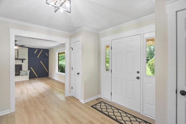 entryway featuring crown molding, light hardwood / wood-style floors, a textured ceiling, and a brick fireplace