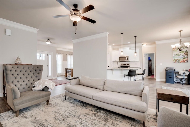 living room with ceiling fan with notable chandelier, sink, light wood-type flooring, and crown molding