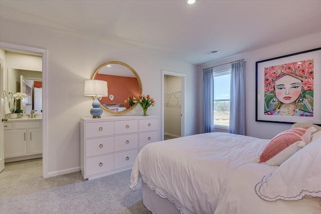 bedroom featuring light carpet, a walk in closet, sink, connected bathroom, and a closet