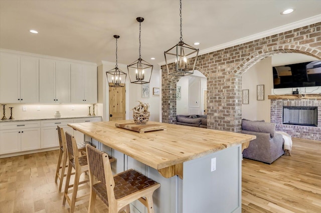 kitchen with pendant lighting, white cabinets, light hardwood / wood-style flooring, a kitchen island, and brick wall