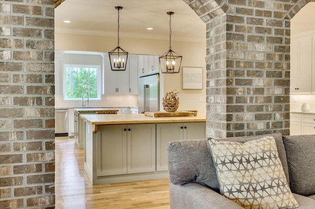 kitchen with pendant lighting, white cabinets, ornamental molding, appliances with stainless steel finishes, and butcher block counters