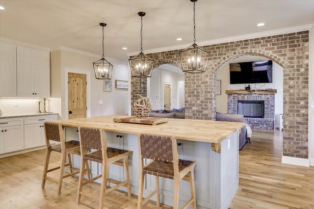 kitchen with white cabinets, decorative light fixtures, a kitchen island, a kitchen bar, and butcher block counters