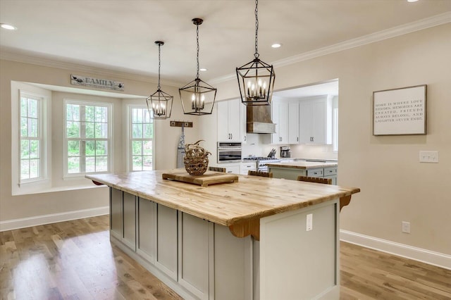 kitchen with appliances with stainless steel finishes, pendant lighting, a center island, light hardwood / wood-style floors, and white cabinetry