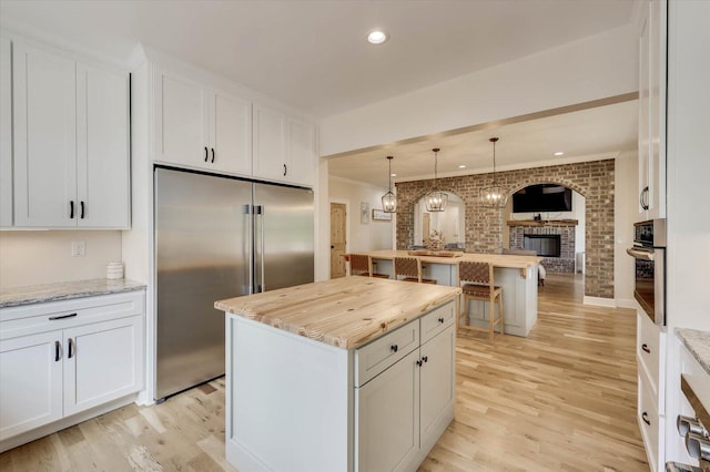 kitchen featuring white cabinets, light stone counters, stainless steel appliances, and brick wall