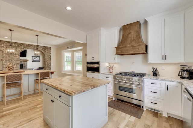 kitchen with white cabinets, a center island, premium range hood, and appliances with stainless steel finishes