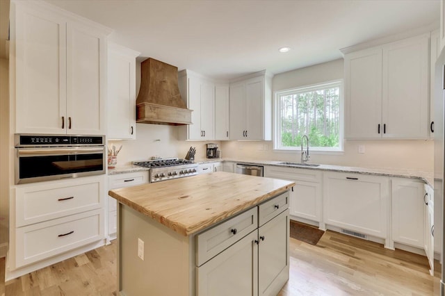 kitchen with custom exhaust hood, stainless steel appliances, a kitchen island, sink, and white cabinetry