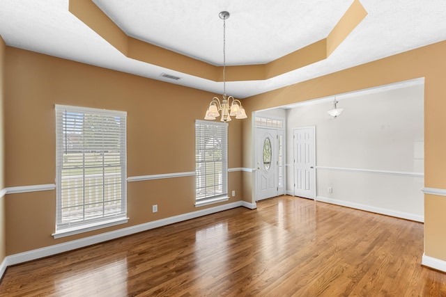 spare room featuring a chandelier, baseboards, wood finished floors, and healthy amount of natural light