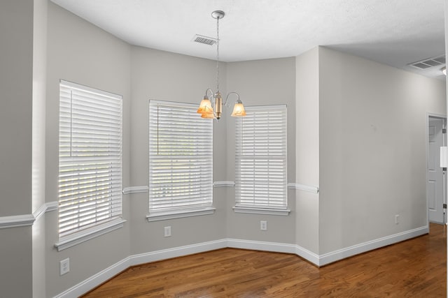 unfurnished dining area with a chandelier, wood finished floors, and baseboards