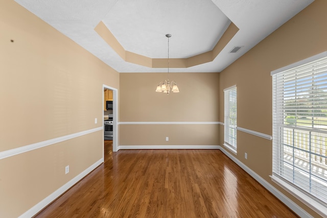 empty room featuring a tray ceiling, wood finished floors, a chandelier, and baseboards