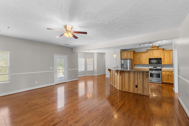 kitchen with appliances with stainless steel finishes, baseboards, open floor plan, ceiling fan, and a textured ceiling