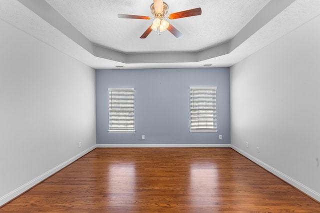empty room with a ceiling fan, a tray ceiling, wood finished floors, a textured ceiling, and baseboards