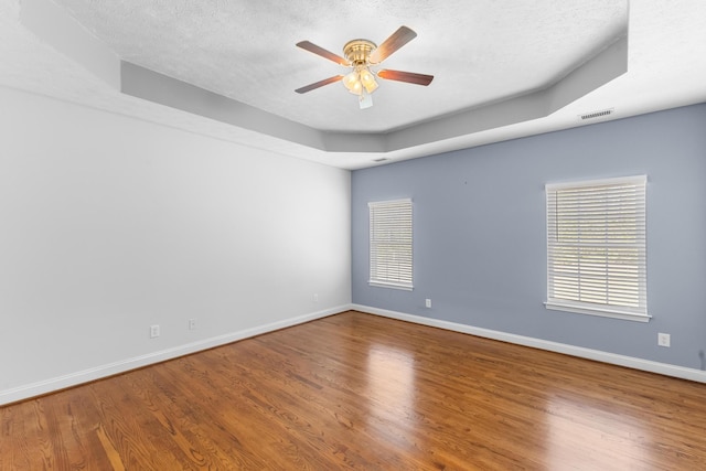unfurnished room with a ceiling fan, a tray ceiling, baseboards, wood finished floors, and a textured ceiling