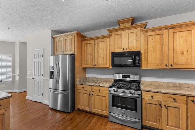kitchen featuring appliances with stainless steel finishes, dark wood-type flooring, a textured ceiling, light stone counters, and baseboards