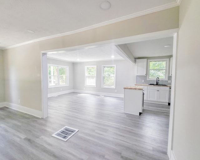 unfurnished living room featuring ornamental molding, sink, and light hardwood / wood-style flooring