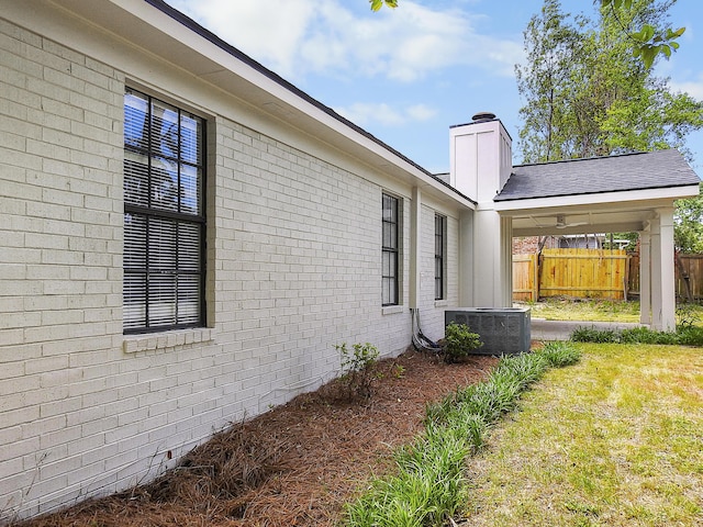 view of property exterior with a chimney, a yard, brick siding, fence, and cooling unit