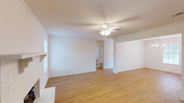 unfurnished living room with ornamental molding, ceiling fan with notable chandelier, a brick fireplace, and plenty of natural light