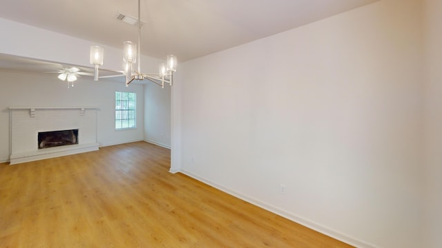 unfurnished living room featuring light wood-style flooring, ceiling fan with notable chandelier, a brick fireplace, baseboards, and visible vents