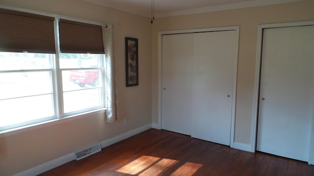 unfurnished bedroom featuring multiple windows, dark wood-type flooring, and ornamental molding