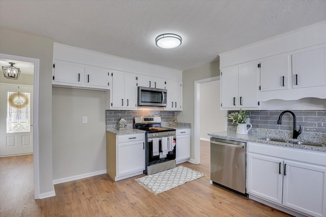 kitchen featuring appliances with stainless steel finishes, backsplash, light stone counters, sink, and white cabinets