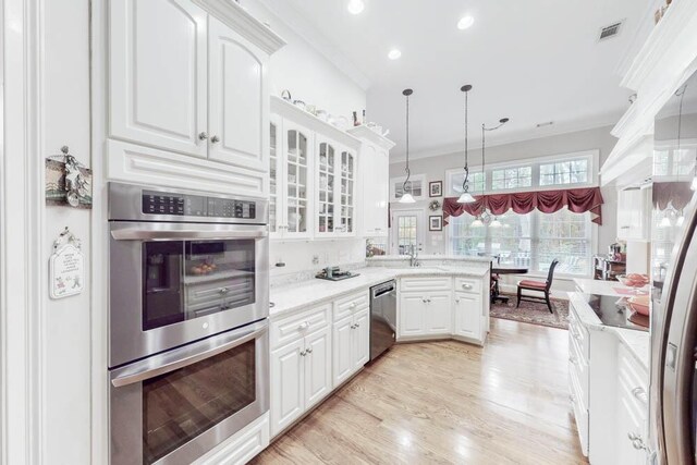 kitchen with white cabinetry, stainless steel appliances, light stone counters, decorative light fixtures, and ornamental molding