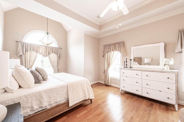bedroom with crown molding, light wood finished floors, a tray ceiling, and multiple windows