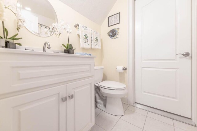 bathroom featuring tile patterned floors, vanity, lofted ceiling, and toilet