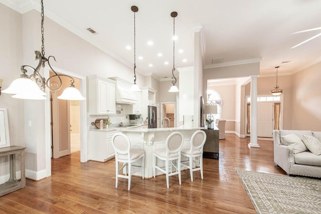 kitchen with white cabinets, a sink, freestanding refrigerator, decorative columns, and a kitchen bar
