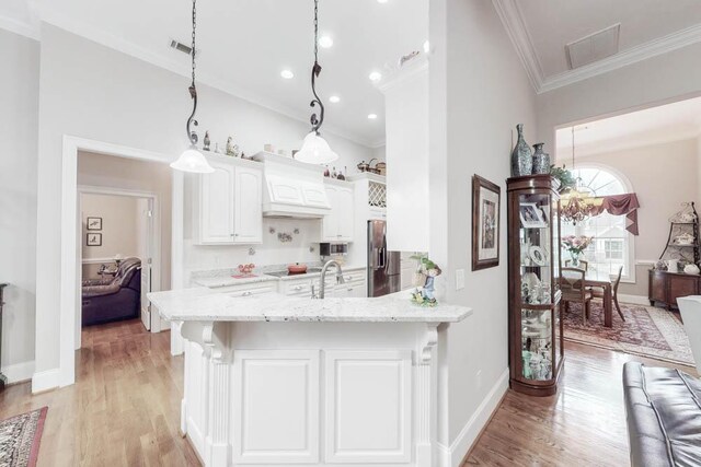 kitchen with custom exhaust hood, white cabinets, crown molding, light stone countertops, and decorative light fixtures