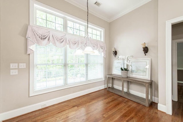 interior space featuring visible vents, wood finished floors, baseboards, a notable chandelier, and ornamental molding